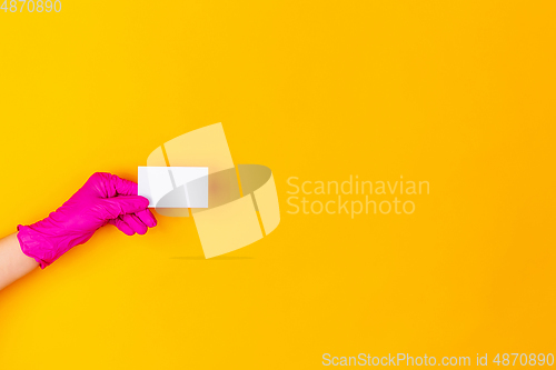 Image of Hand in pink rubber glove holding business card isolated on yellow studio background with copyspace.