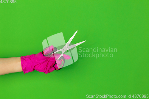 Image of Hand in pink rubber glove holding sccissors isolated on green studio background with copyspace.