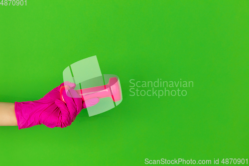 Image of Hand in pink rubber glove holding gym weight, dumbbell isolated on green studio background with copyspace.