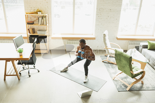 Image of Young african-american man training at home during quarantine of coronavirus outbreak, doinc exercises of fitness, aerobic. Staying sportive suring insulation.