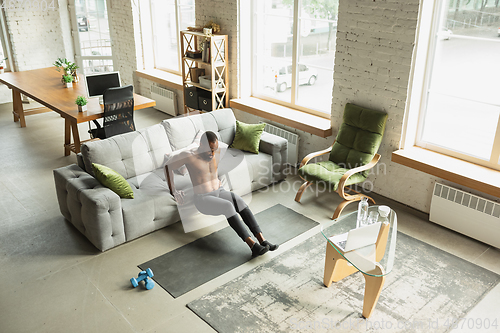 Image of Young african-american man training at home during quarantine of coronavirus outbreak, doinc exercises of fitness, aerobic. Staying sportive suring insulation.