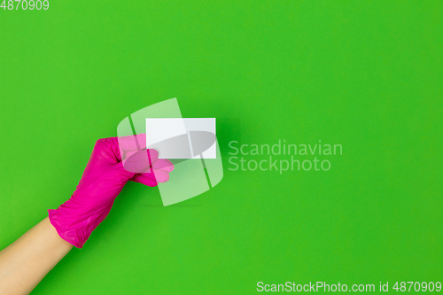 Image of Hand in pink rubber glove holding business card isolated on green studio background with copyspace.