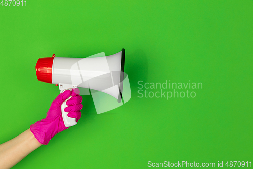 Image of Hand in pink rubber glove holding megaphone isolated on green studio background with copyspace.