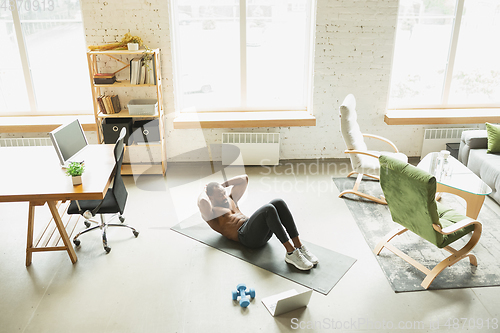 Image of Young african-american man training at home during quarantine of coronavirus outbreak, doinc exercises of fitness, aerobic. Staying sportive suring insulation.