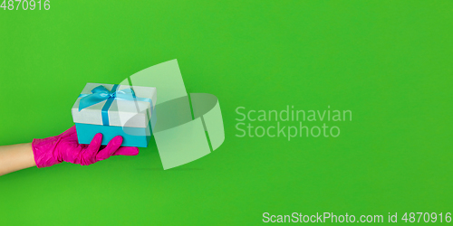 Image of Hand in pink rubber glove holding giftbox isolated on green studio background with copyspace. Flyer, proposal.