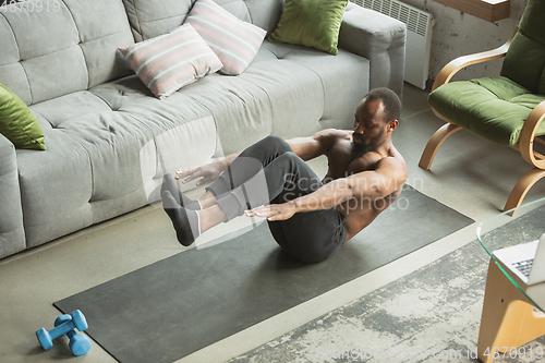 Image of Young african-american man training at home during quarantine of coronavirus outbreak, doinc exercises of fitness, aerobic. Staying sportive suring insulation.