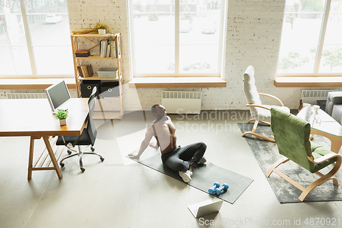 Image of Young african-american man training at home during quarantine of coronavirus outbreak, doinc exercises of fitness, aerobic. Staying sportive suring insulation.