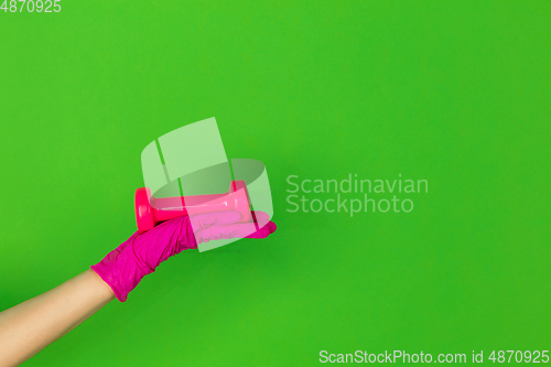 Image of Hand in pink rubber glove holding gym weight, dumbbell isolated on green studio background with copyspace.