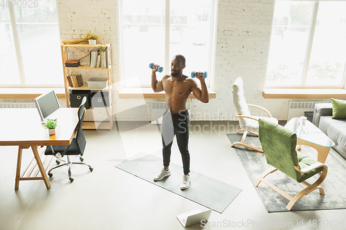 Image of Young african-american man training at home during quarantine of coronavirus outbreak, doinc exercises of fitness, aerobic. Staying sportive suring insulation.