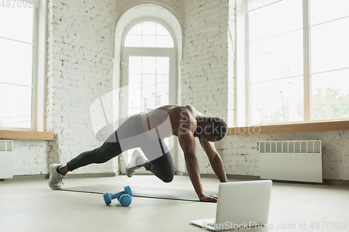 Image of Young african-american man training at home during quarantine of coronavirus outbreak, doinc exercises of fitness, aerobic. Staying sportive suring insulation.