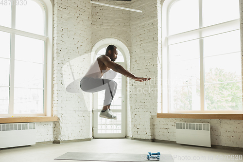 Image of Young african-american man training at home during quarantine of coronavirus outbreak, doinc exercises of fitness, aerobic. Staying sportive suring insulation.