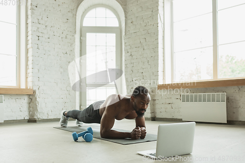 Image of Young african-american man training at home during quarantine of coronavirus outbreak, doinc exercises of fitness, aerobic. Staying sportive suring insulation.