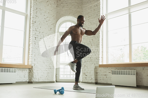 Image of Young african-american man training at home during quarantine of coronavirus outbreak, doinc exercises of fitness, aerobic. Staying sportive suring insulation.