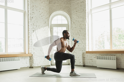 Image of Young african-american man training at home during quarantine of coronavirus outbreak, doinc exercises of fitness, aerobic. Staying sportive suring insulation.