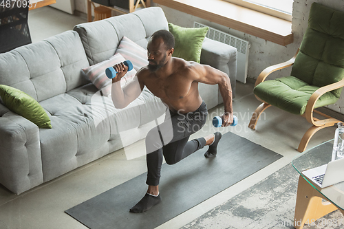 Image of Young african-american man training at home during quarantine of coronavirus outbreak, doinc exercises of fitness, aerobic. Staying sportive suring insulation.