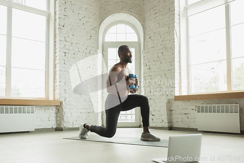 Image of Young african-american man training at home during quarantine of coronavirus outbreak, doinc exercises of fitness, aerobic. Staying sportive suring insulation.