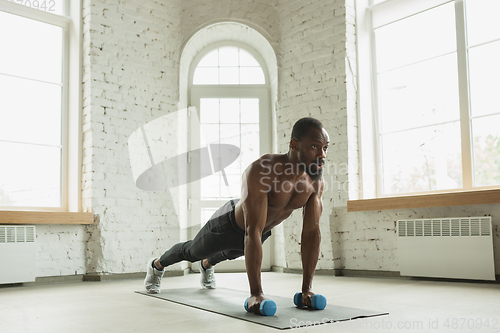 Image of Young african-american man training at home during quarantine of coronavirus outbreak, doinc exercises of fitness, aerobic. Staying sportive suring insulation.