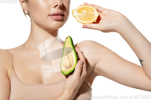 Image of Vitamins. Close up of beautiful young woman with avocado and orange halfs over white background. Cosmetics and makeup, natural and eco treatment, skin care.