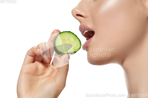 Image of Freshness. Close up of beautiful young woman biting cucumber\'s slice over white background. Cosmetics and makeup, natural and eco treatment, skin care.