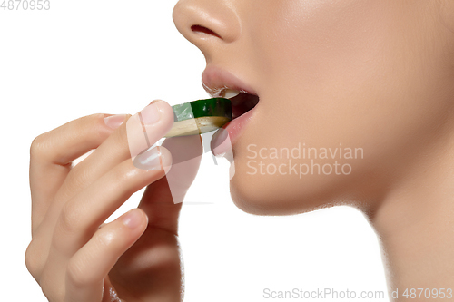 Image of Freshness. Close up of beautiful young woman biting cucumber\'s slice over white background. Cosmetics and makeup, natural and eco treatment, skin care.