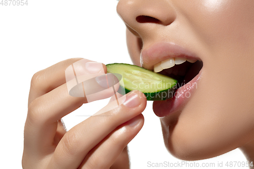 Image of Freshness. Close up of beautiful young woman biting cucumber\'s slice over white background. Cosmetics and makeup, natural and eco treatment, skin care.