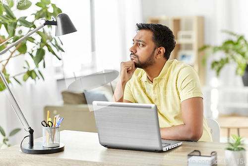 Image of indian man with laptop thinking at home office