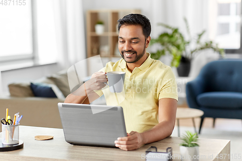 Image of man with laptop drinking coffee at home office