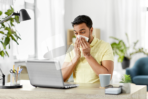 Image of indian man with laptop blowing nose at home office