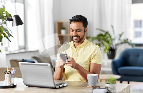 Image of happy indian man with smartphone at home office