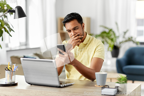 Image of happy indian man with smartphone at home office