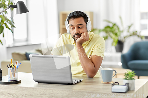 Image of bored man in headphones with laptop works at home