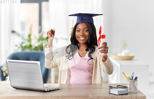 Image of graduate student with laptop and diploma at home