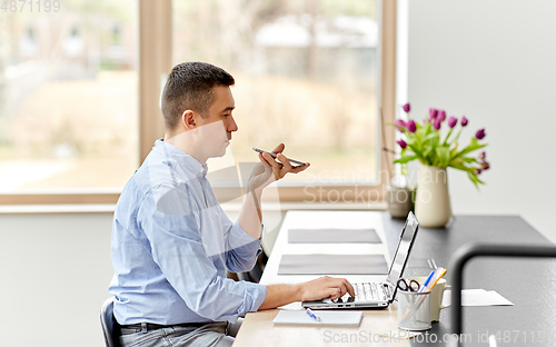 Image of man with smartphone and laptop at home office