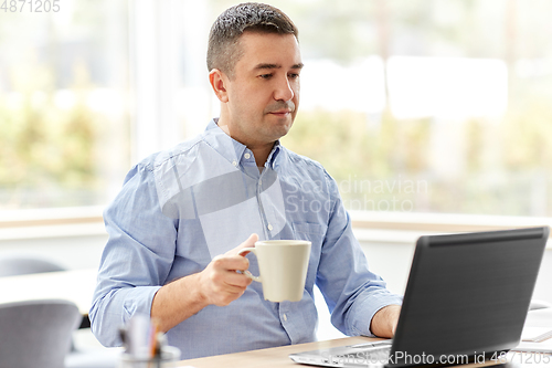 Image of man with laptop drinking coffee at home office