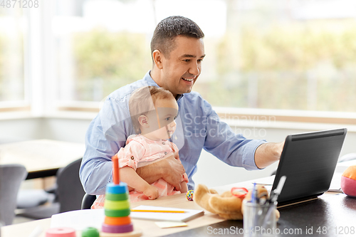 Image of father with baby working on laptop at home office