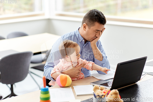 Image of father with baby working on laptop at home office