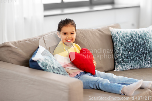 Image of happy little girl with heart shaped pillow at home