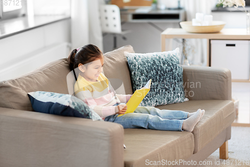 Image of happy smiling little girl reading book at home