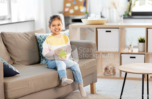 Image of happy little girl with apple sitting on sofa