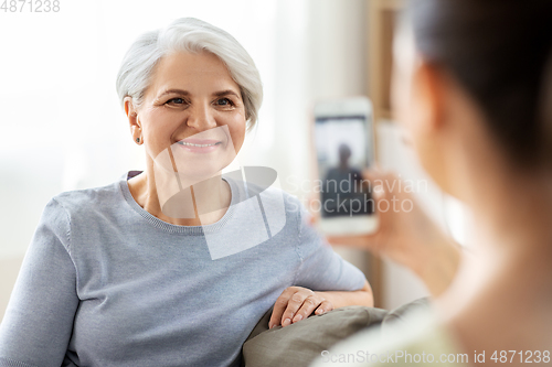 Image of adult daughter photographing senior mother at home