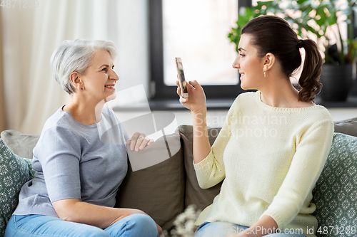 Image of adult daughter photographing senior mother at home