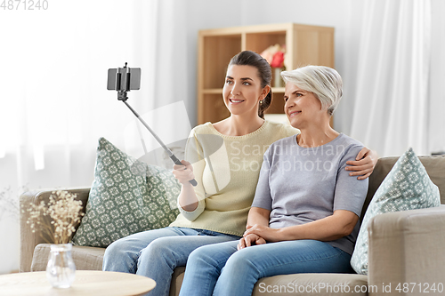 Image of senior mother with daughter taking selfie at home