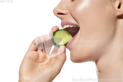 Image of Freshness. Close up of beautiful young woman biting cucumber\'s slice over white background. Cosmetics and makeup, natural and eco treatment, skin care.