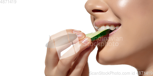 Image of Freshness. Close up of beautiful young woman biting cucumber\'s slice over white background. Cosmetics and makeup, natural and eco treatment, skin care. Flyer, proposal.