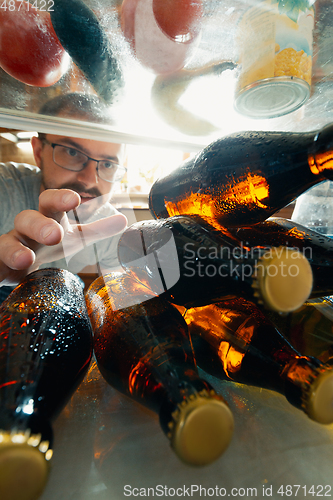 Image of Caucasian man takes cold refreshing beer from out the fridge, inside view from fridge of hand holding the bottle