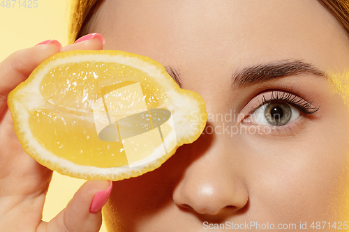 Image of Close up of beautiful female face with lemon slice over yellow background. Cosmetics and makeup, natural and eco treatment, skin care.