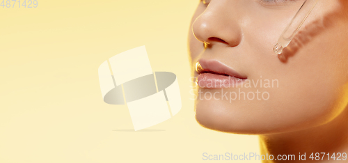 Image of Close up of beautiful young woman with essential oil pouring over yellow background. Cosmetics and makeup, natural and eco treatment, skin care. Flyer with copyspace.