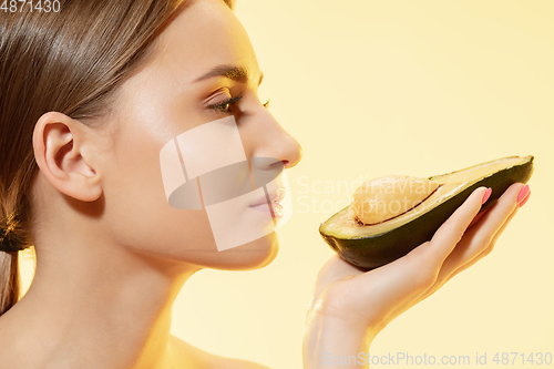 Image of Close up of beautiful female face with half avocado over yellow background. Cosmetics and makeup, natural and eco treatment, skin care.