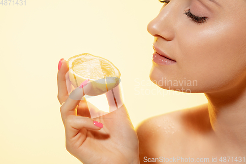 Image of Close up of beautiful female face with lemon slice over yellow background. Cosmetics and makeup, natural and eco treatment, skin care.