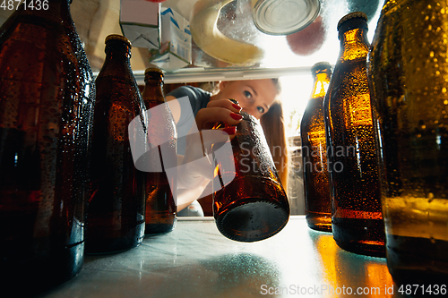 Image of Caucasian woman takes cold refreshing beer from out the fridge, inside view from fridge of hand holding the bottle